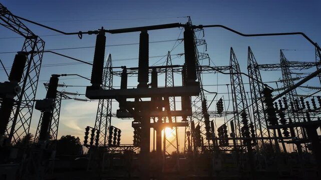 Silhouettes of electrical parts and structural elements of a power station at sunset. the sun appears and disappears through the structure due to the movement of the camera.
