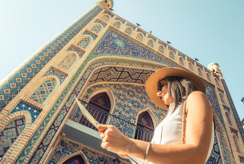 Smiling female tourist with map by colorful islamic architecture Persian-style mosque building. Travel sightseeing planning, cultural discovery, solo journey, heritage adventure