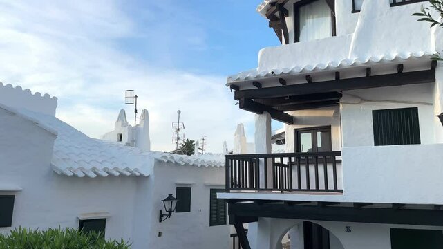 Traditional whitewashed houses of Binibeca Vell, Menorca, with shutters and wooden balconies under a blue sky. A charming Mediterranean village with peaceful architecture.
