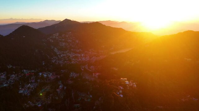 Aerial drone shot displaying sunrays breaking through the clouds, illuminating the Nainital mountains.