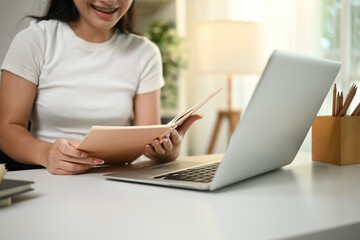 Fototapeta premium Close-up of a teenage girl reading a textbook while studying at a bright home workspace, Focused on online learning and self-study
