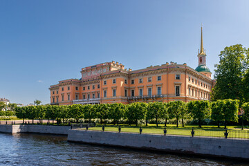 Mikhailovsky Castle with a golden spire rises above the river, surrounded by a row of green trees.