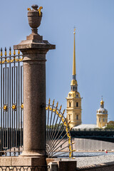 A close-up of a granite column and a forged grille of the Summer Garden fence, with the spire of the Peter and Paul Fortress visible in the background.