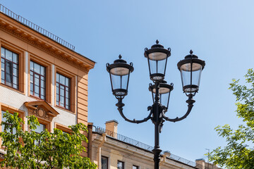 A street lamp with four shades against the background of an old building and a blue sky in the city.