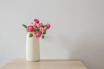 pink roses in ceramic vase on wooden table  in white interior