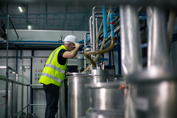 A male industrial engineer wearing a safety helmet and reflective vest is inspecting equipment in a...