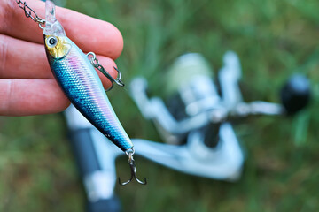 Wobbler in the hand of a fisherman on the background of a spinning reel. Fishing tackle. Selective focus