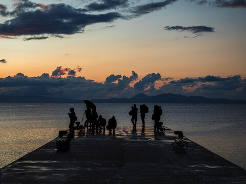silhouettes of people at sunset after rain on the seashore, on the pier