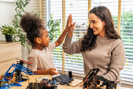 Excited mother and daughter giving a high five after successfully assembling a robotics project, STEM activities that inspire creativity, and early engineering skills, fostering problem-solving skills