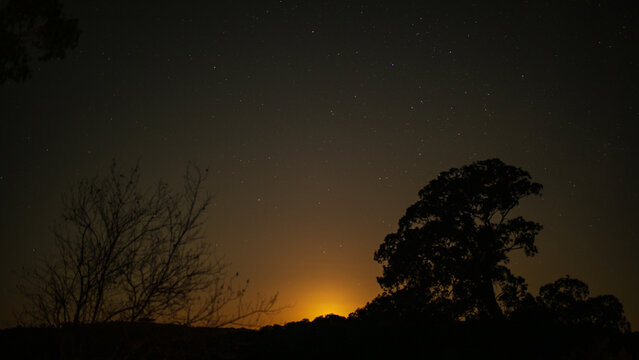 Starlit sky over rural Australian landscape with golden glow of rising moon beneath the horizon
