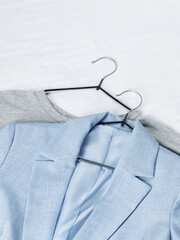 A light blue jacket hangs on a hanger next to a gray one