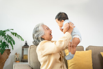 Happy Asian Grandmother Playing with Grandchild at Home, Joyful Senior Woman Lifting and Bonding with Infant Baby, Multi Generational Family Love, Grandma and Baby Fun