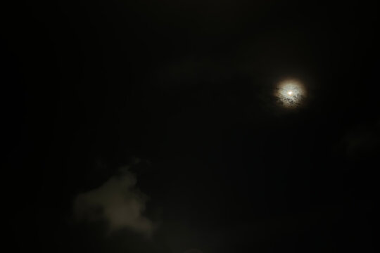 The night sky features a black background contrasted by the soft white-yellow glow of the moon, adorned with clusters of gray cloud