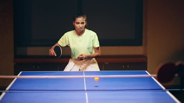 Indian happy young adult gen z athlete player woman hold racket play table tennis male man passing ball indoor dark room Asian sporty girl lady do sports training enjoy ping pong game have fun joy