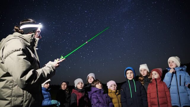 Astronomer with headlamp points laser at stars, teaching astronomy to children during a stargazing night