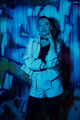Obraz premium Stylish woman posing confidently against a vibrant urban graffiti backdrop at night