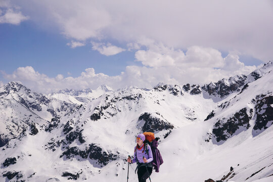 A young woman with a backpacker stands in the snowy mountains. Hiking and trekking in the mountains