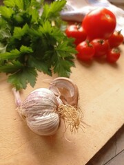 Close up of some garlic, a bunch of flat-leaf parsley and a few tomatoes on a wooden cutting board with a kitchen towel. 