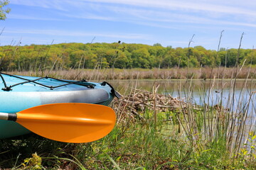 Blue kayak rests on the shore of a river next to a beaver lodge © John Outdoors