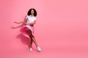 Young African American woman dancing happily in a casual pink outfit on a vibrant pink studio...