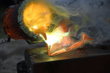 flüssiges Metall gießen aus rotglühendem, rauchendem Schmelztiegel mit lodernden Flammen