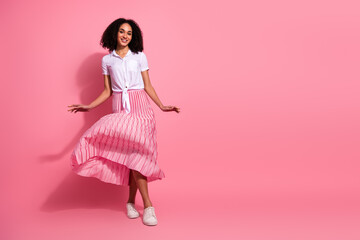 Young stylish woman in casual outfit posing against pink background, wearing pleated skirt,...