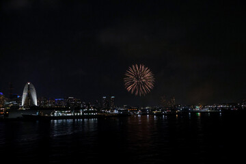 Fireworks explode in the sky over Yokohama Port, with the city skyline in the background