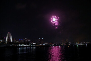 Fototapeta premium Fireworks explode in the sky over Yokohama Port, with the city skyline in the background