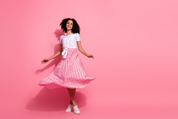 Elegant young woman in pink pleated skirt posing confidently against solid pink background in cheerful studio shoot