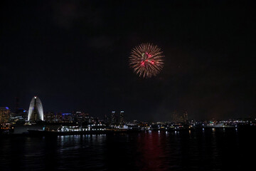 Fireworks explode in the sky over Yokohama Port, with the city skyline in the background