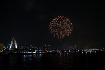 Fireworks explode in the sky over Yokohama Port, with the city skyline in the background