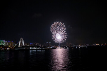 Fireworks explode in the sky over Yokohama Port, with the city skyline in the background