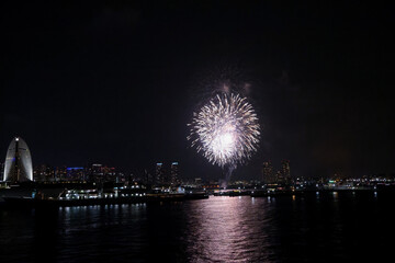 Fireworks explode in the sky over Yokohama Port, with the city skyline in the background