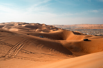 golden sand dunes of the Liwa Festival desert in Abu Dhabi. Tracks in the sand lead to a distant encampment, blending festival energy with serene desert beauty