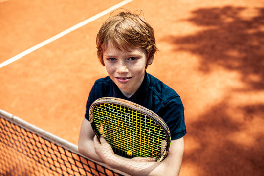Portrait of a young boy smiling on a tennis court with a racket