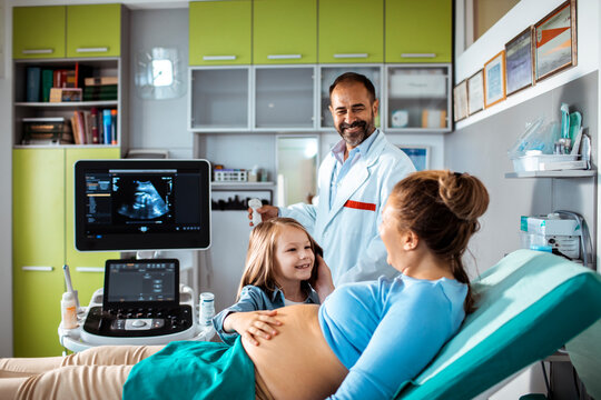 Pregnant woman with daughter and doctor during ultrasound appointment at clinic