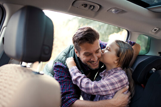 Father kissing little daughter on forehead while adjusting her seatbelt in car