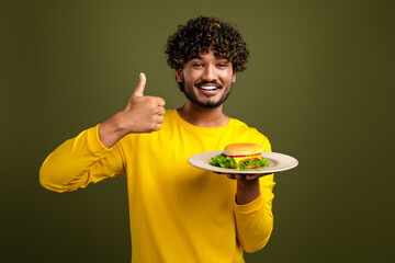 Young man in vibrant yellow attire smiling with enthusiasm while holding a homemade burger on...