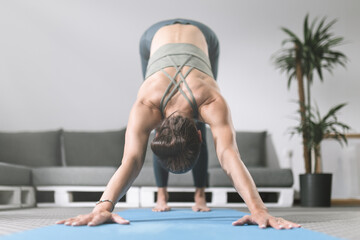 Woman practicing downward-facing dog yoga pose in modern living room setting