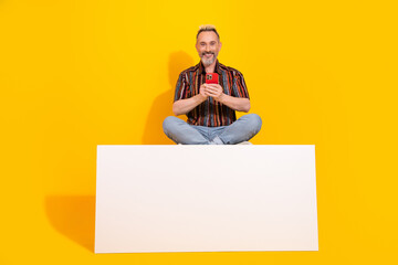 Mature charismatic gentleman holding smartphone on yellow backdrop showcasing style and happiness