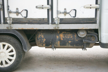 Close-up view of a weathered truck's undercarriage showcasing a rusty gas tank and wheel, highlighting the wear and tear of industrial vehicles in urban environments