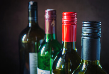 Close-up of metal cap on dark glass wine bottle, variety of wine bottles are lined up.