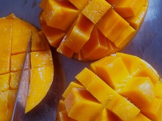 Closeup of three halved mangos cutting with knife in slice. Mango slices are a great addition to smoothies, adding sweetness and tropical flavor. 