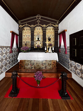 Wide shot of a traditional Catholic chapel interior showing the altar on a raised wooden platform, framed by azulejo tiled walls, white plaster, and a red carpet runner in the foreground.