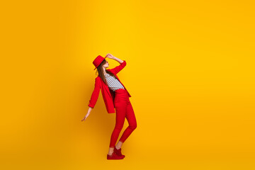 Young stylish woman in red suit and hat posing on bright yellow background for trendy fashion and...