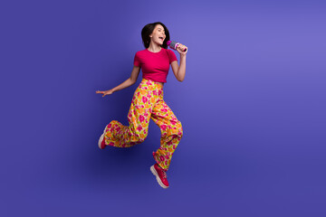 Smiling young woman in colorful pants enthusiastically singing while holding a microphone on a...