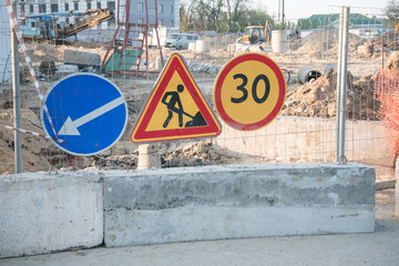 Construction site with traffic signs indicating direction and speed limit near urban area during daylight hours