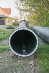 Large drainage pipe rests on grassy area near residential buildings in natural light during late afternoon hours