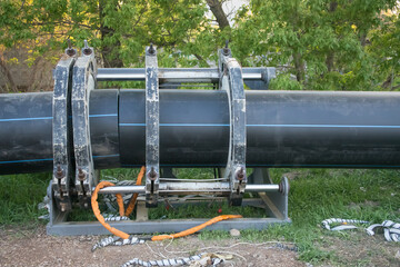 Large black pipeline installation process in a green area during daylight hours
