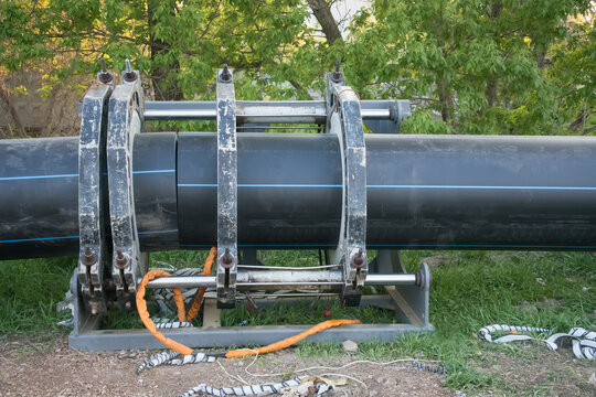 Large black pipeline installation process in a green area during daylight hours